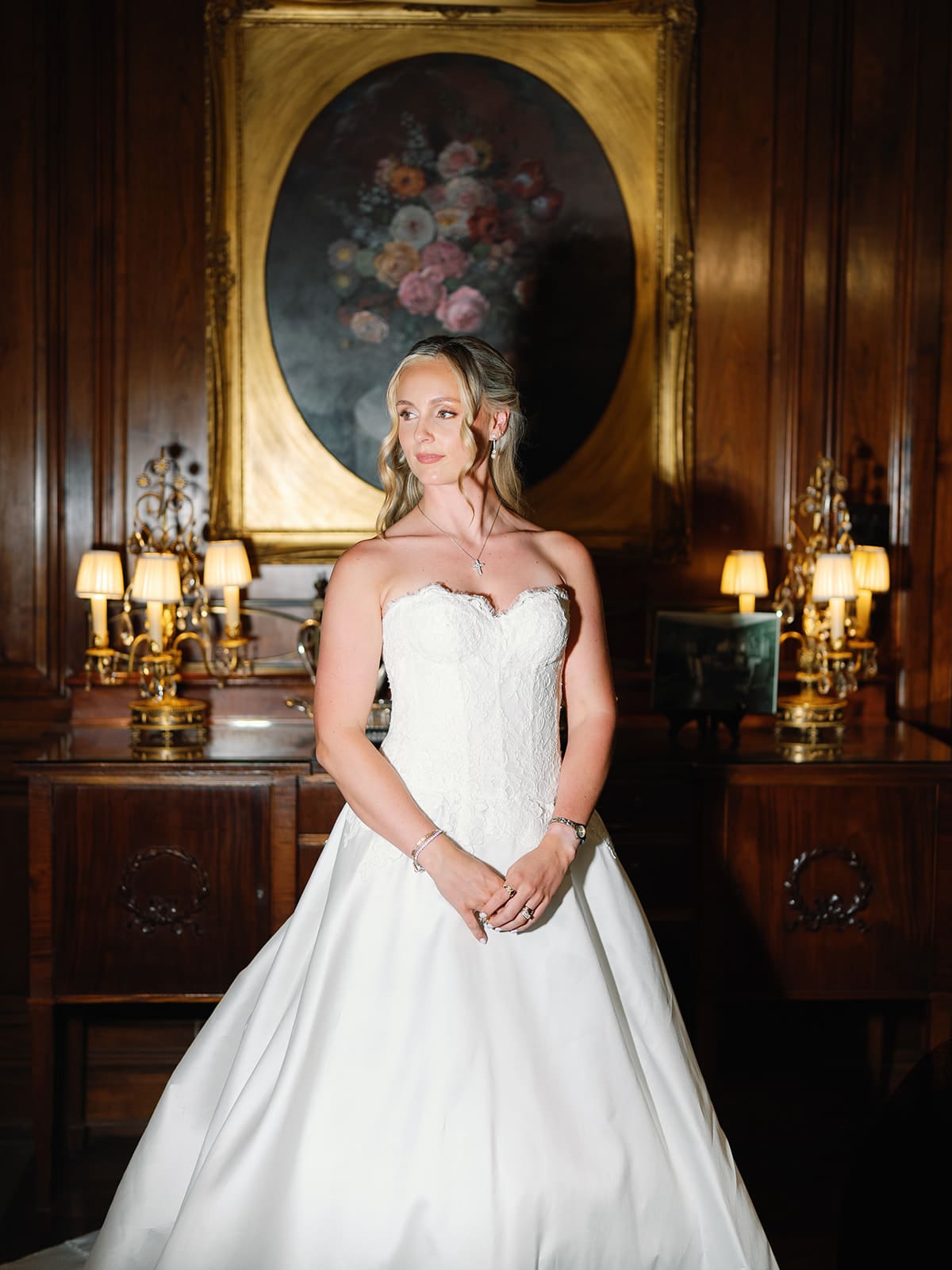 Bride standing in wedding dress in front of oil painting of flowers